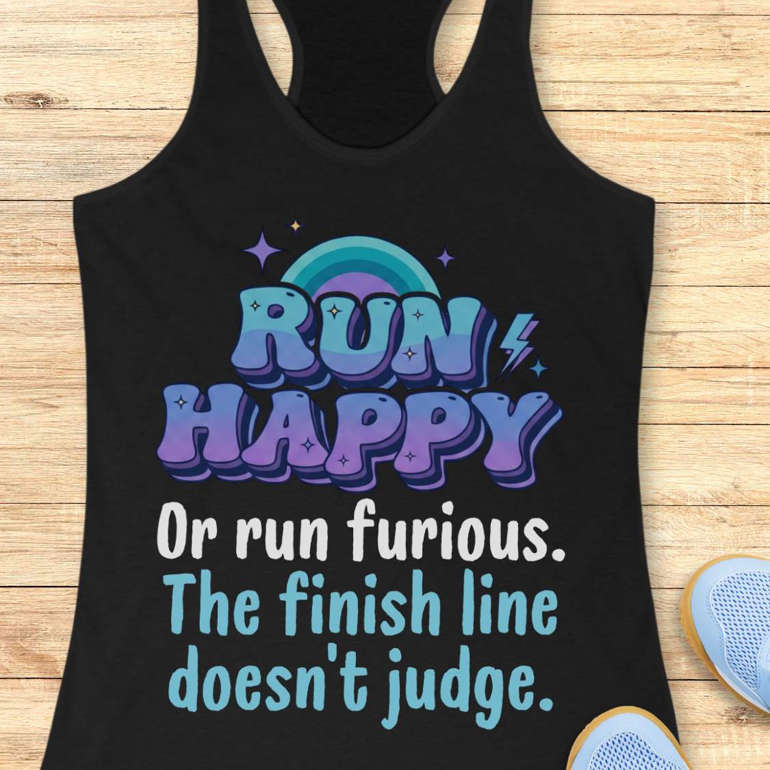 Black tank top with colorful text "RUN HAPPY OR RUN FURIOUS. THE FINISH LINE DOESN'T JUDGE. " and rainbow design on a wooden surface