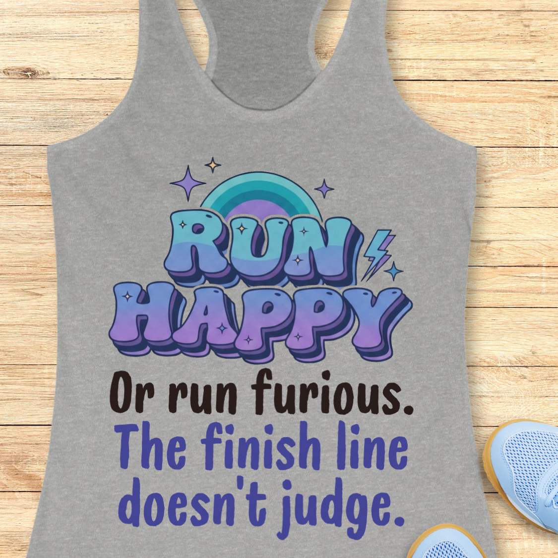 Gray tank top with colorful text  "RUN HAPPY OR RUN FURIOUS. THE FINISH LINE DOESN'T JUDGE. " and rainbow design on a wooden surface