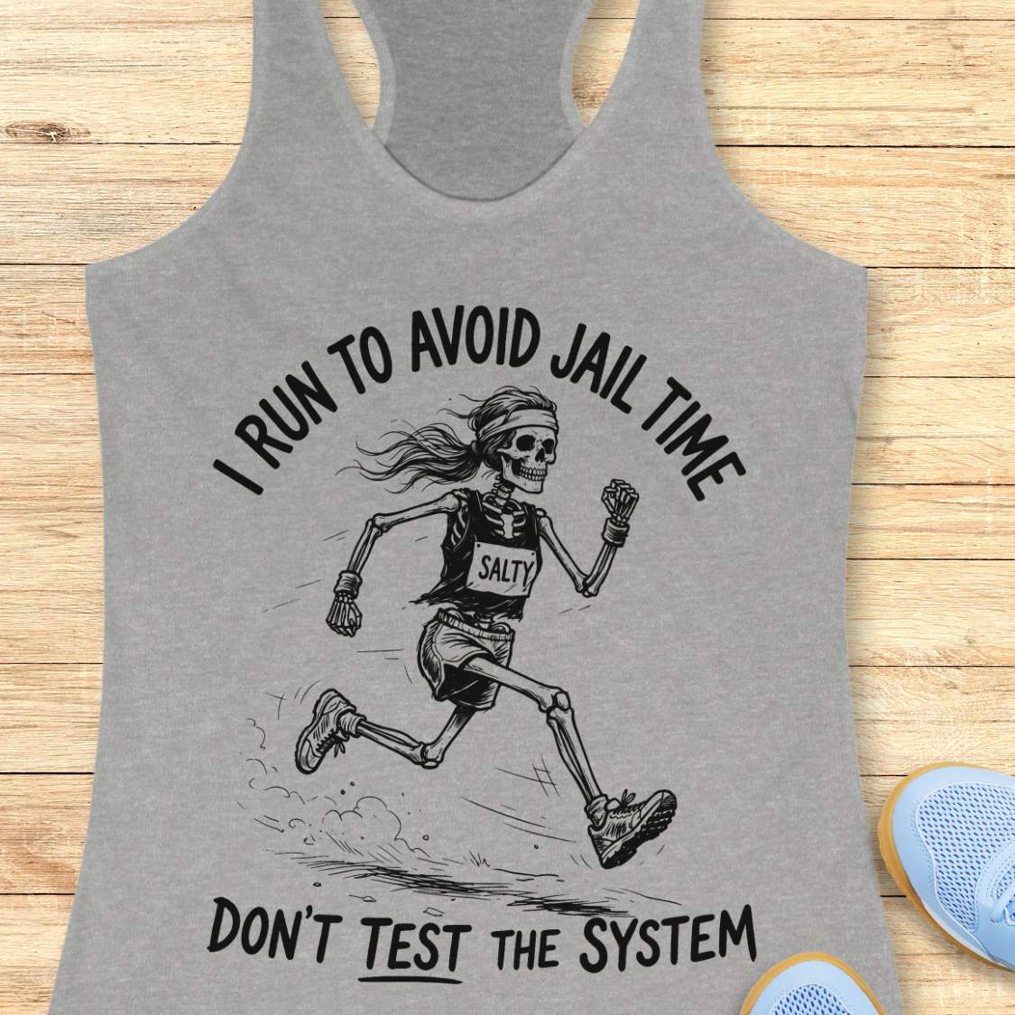 Gray tank top with skeleton running graphic and text i run to avoid jail time don't test the system  on a wooden surface