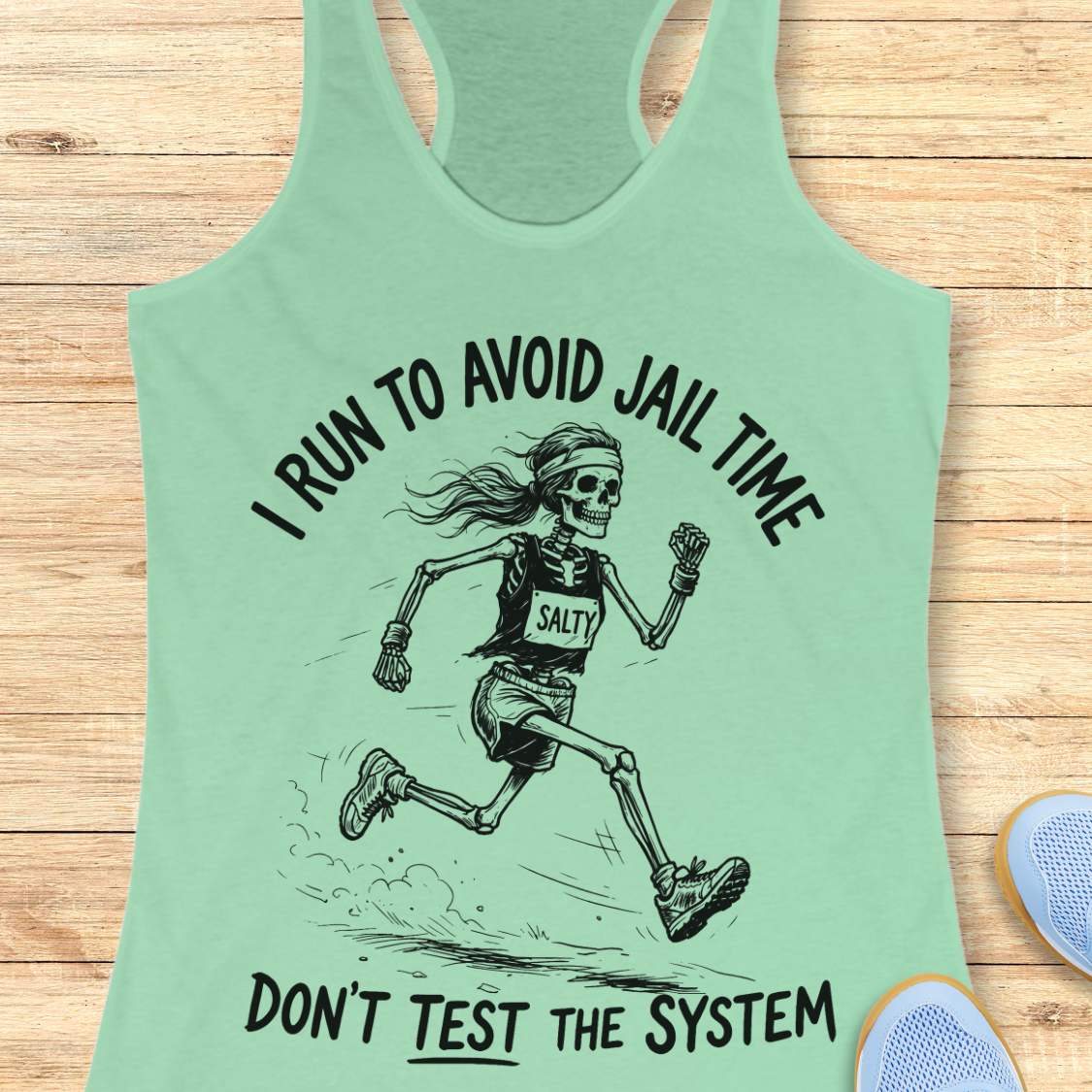 Mint green tank top with skeleton graphic and text i run to avoid jail time don't test the system  on a wooden surface