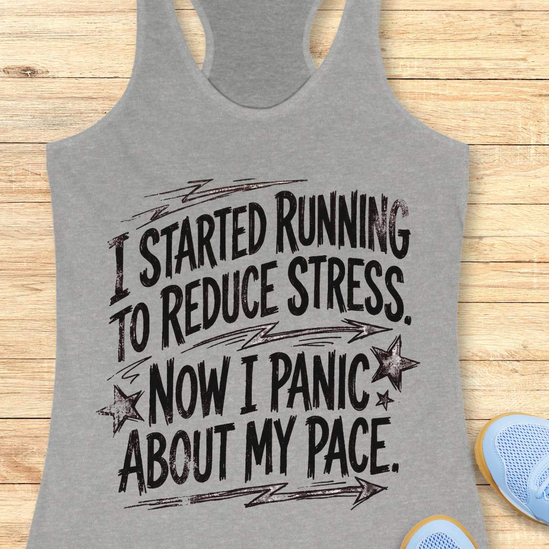 Gray tank top with humorous text I started running to reduce stress. Now I panic about my pace.  on a wooden surface