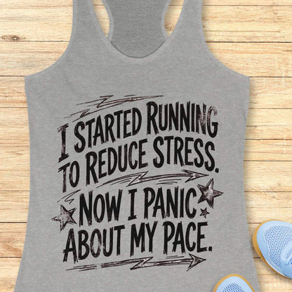Gray tank top with humorous text I started running to reduce stress. Now I panic about my pace.  on a wooden surface