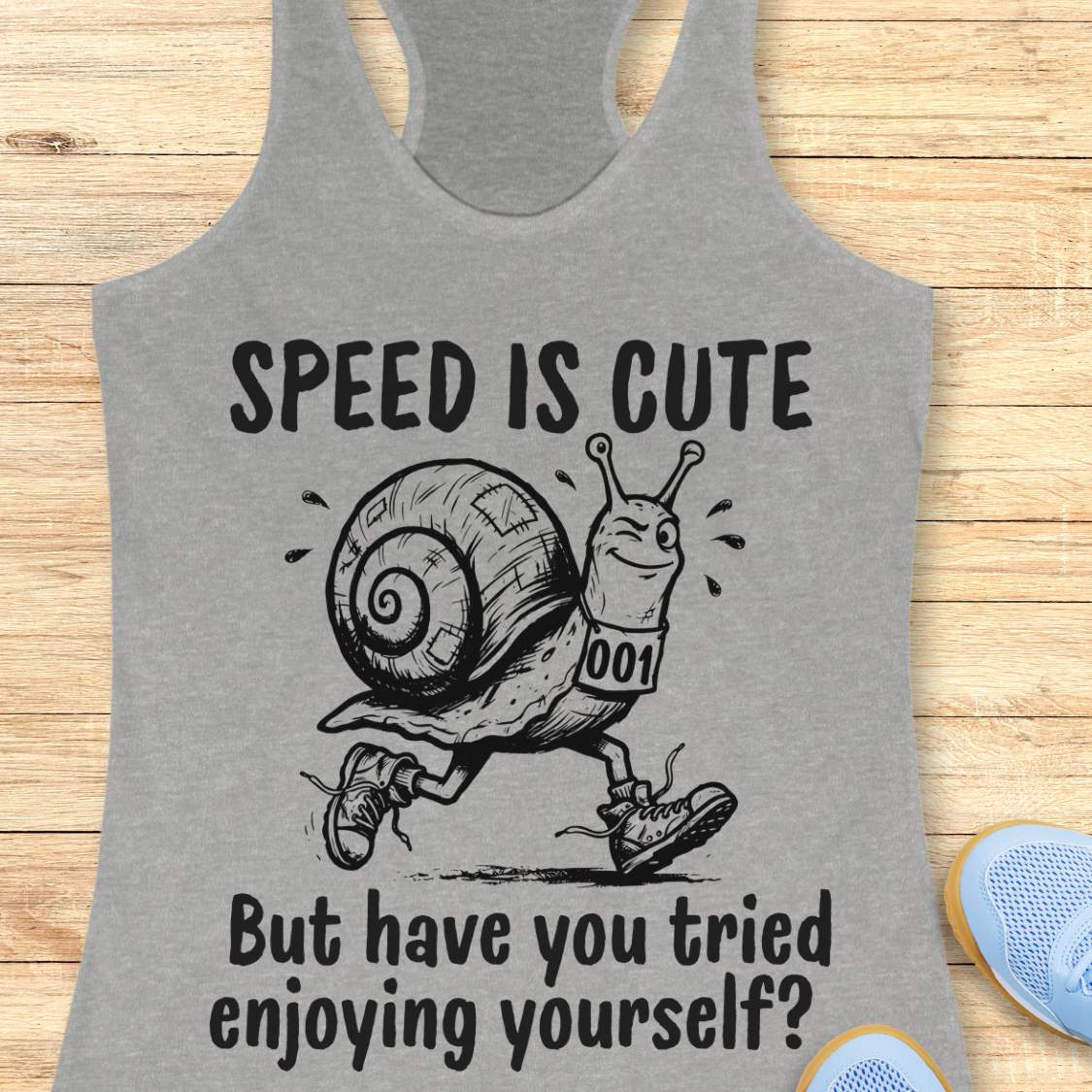 grey tank top with a snail image and text - speed is cute but have you tried enjoying yourself? on a wooden background