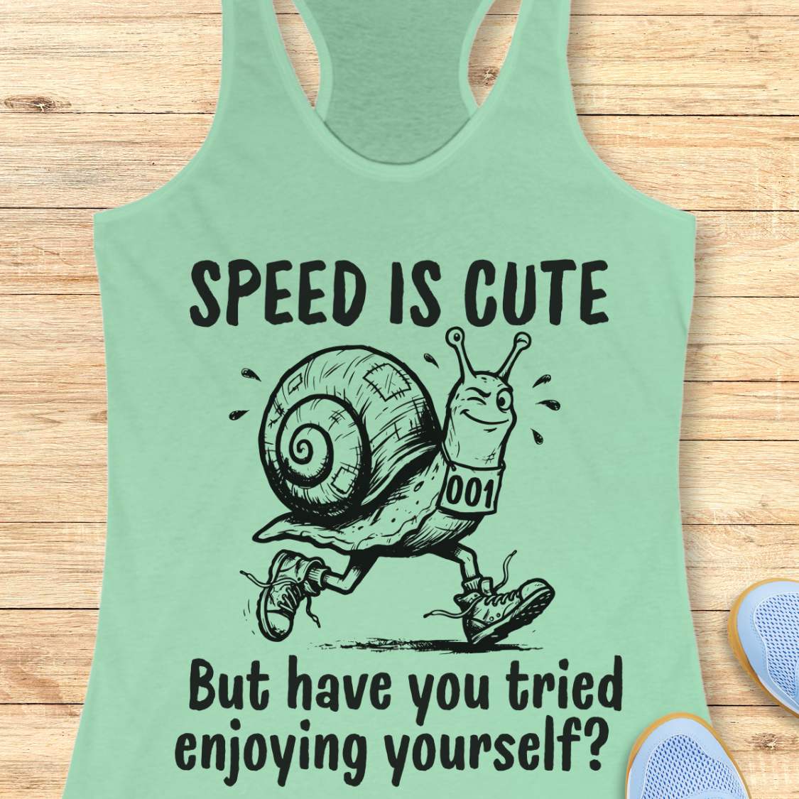 mint tank top with a snail image and text - speed is cute but have you tried enjoying yourself? on a wooden background