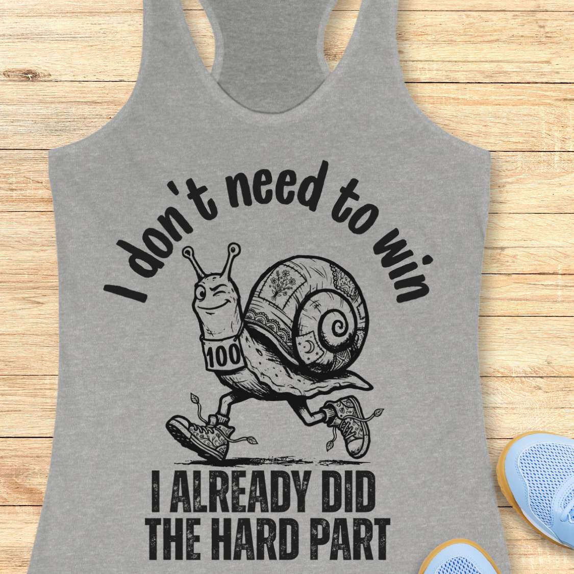 grey tank top with an image of  snail and text - I don't need to win I already did the hard part, on a wooden background