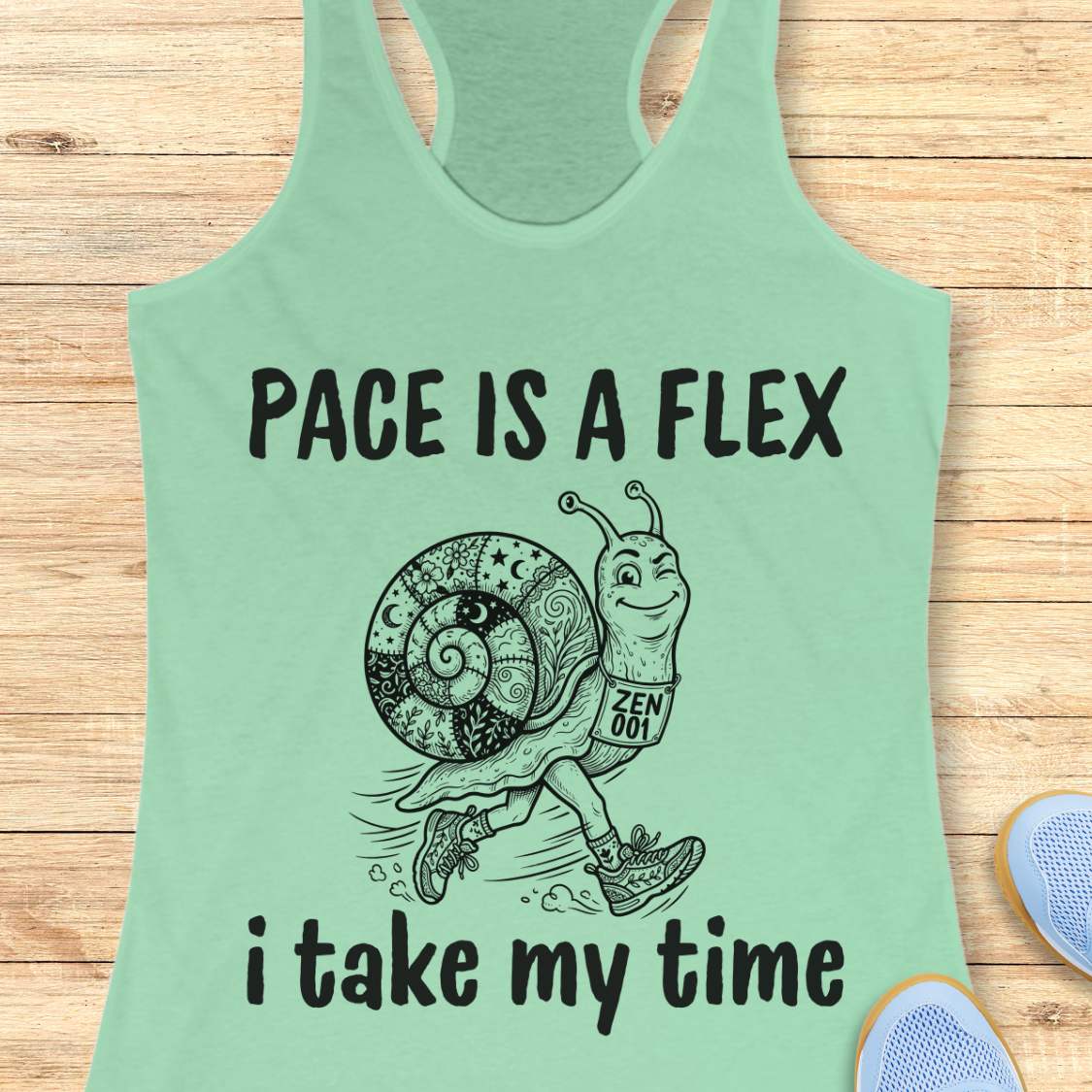Mint green tank top with a snail graphic and text pace is a flex , i take my time, on a wooden surface