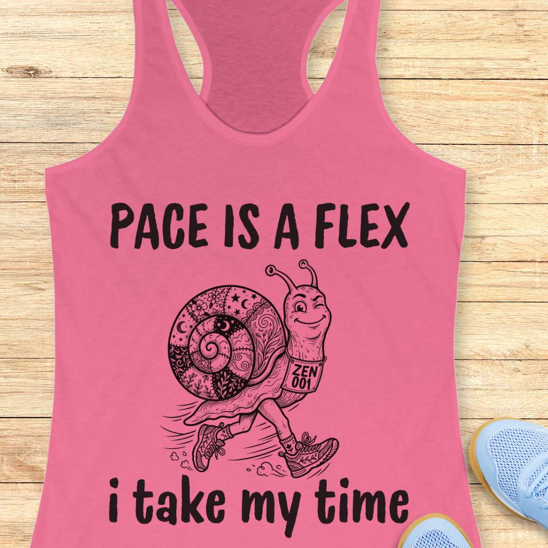 Pink tank top with a snail graphic and text pace is a flex , i take my time, on a wooden surface