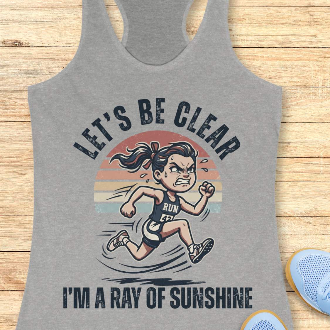 Gray tank top with a graphic of a running person and text let's be clear, I'm a ray of sunshine on a wooden surface