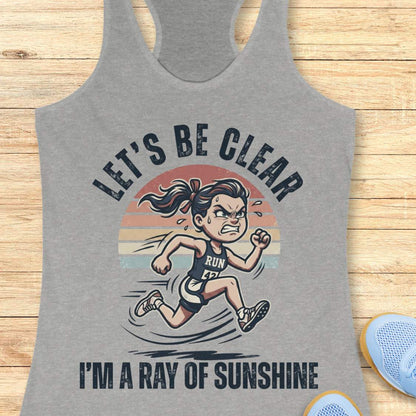 Gray tank top with a graphic of a running person and text let's be clear, I'm a ray of sunshine on a wooden surface