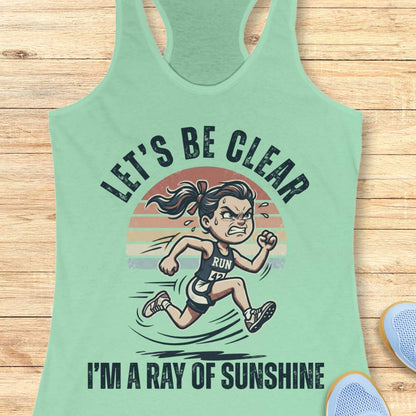 Light green tank top with a graphic of a running person and text let's be clear, I'm a ray of sunshine on a wooden surface