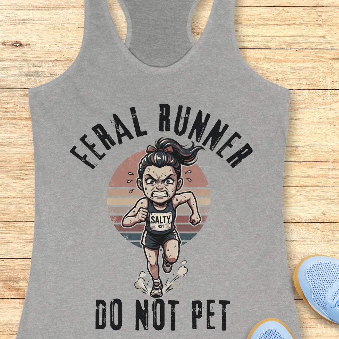 Gray tank top with a graphic of a running woman and text feral runner do not pet on a wooden surface