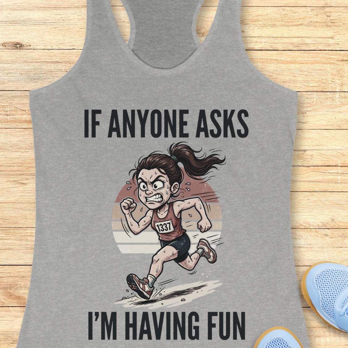 Gray tank top with cartoon graphic and text 'If anyone asks I'm having fun' on a wooden surface.