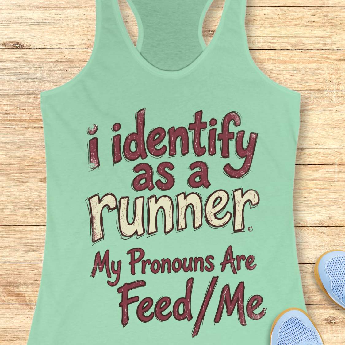 Mint green tank top with text 'i identify as a runner My Pronouns Are Feed/Me' on a wooden surface