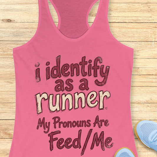 Pink tank top with text 'i identify as a runner My Pronouns Are Feed/Me' on a wooden surface