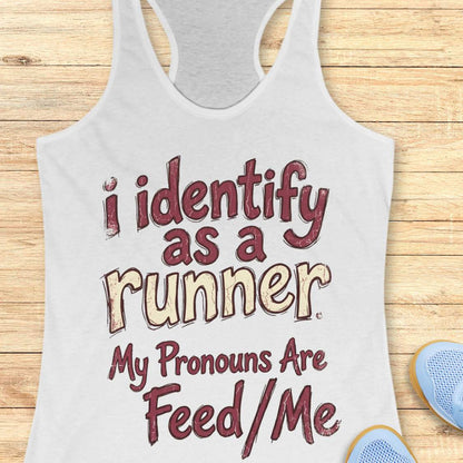 White tank top with text 'i identify as a runner. My pronouns are feed/me' on a wooden surface.