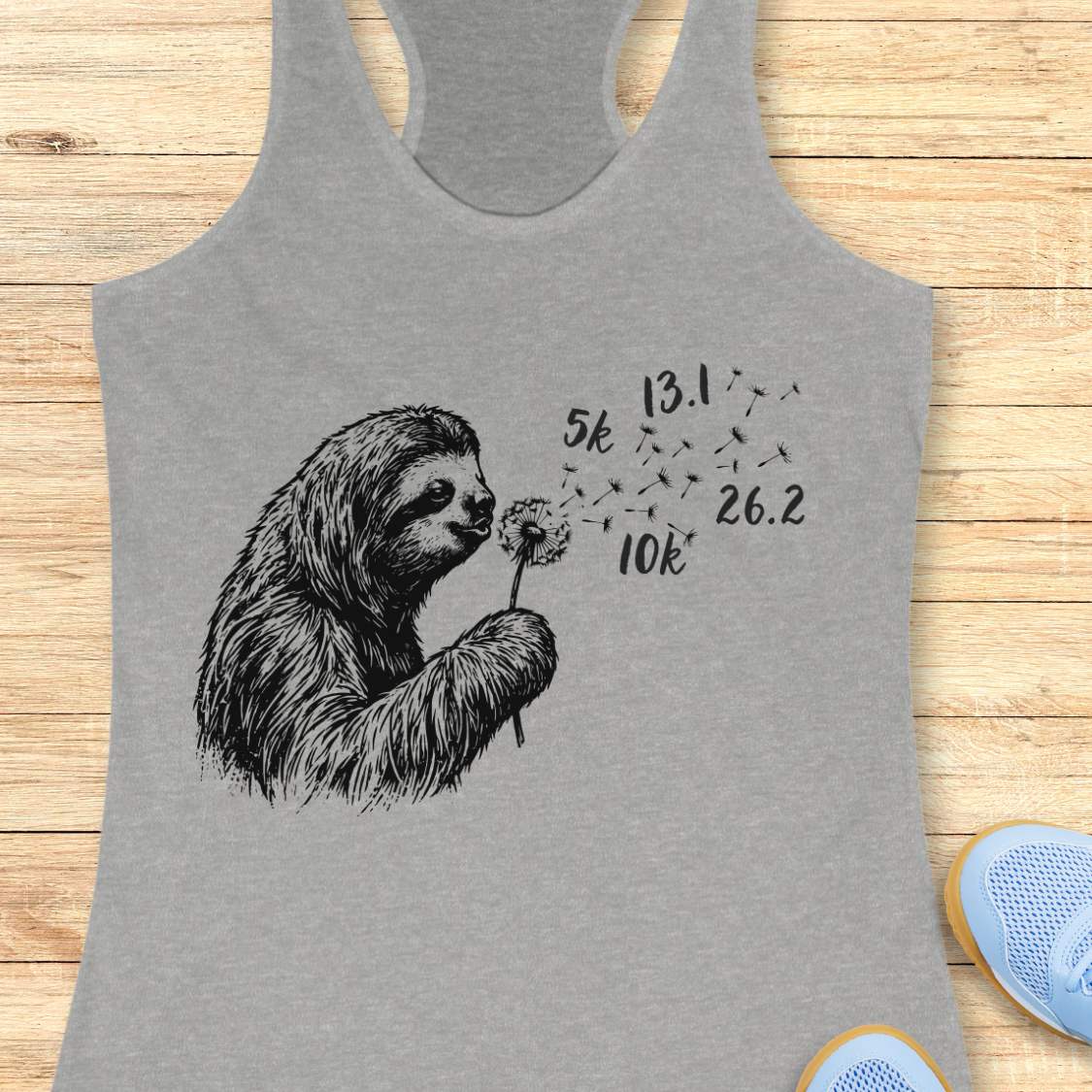 Gray tank top with a sloth holding a dandelion on a wooden surface