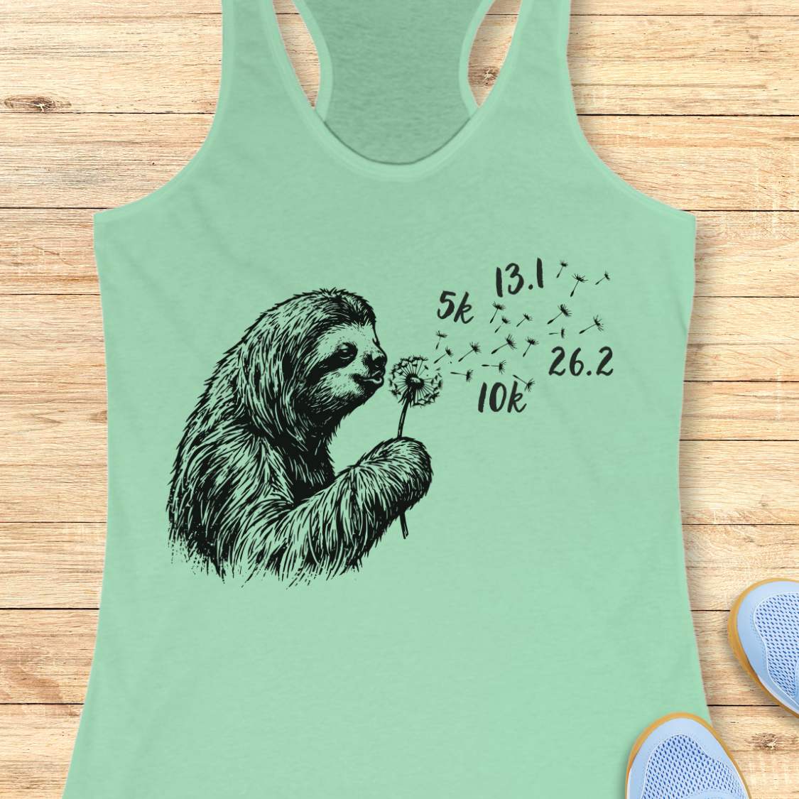Light green tank top with a sloth graphic and running distances on a wooden surface
