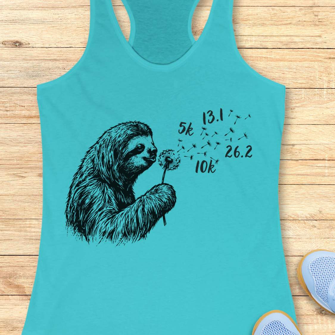 Turquoise tank top with a sloth blowing dandelion design on a wooden surface
