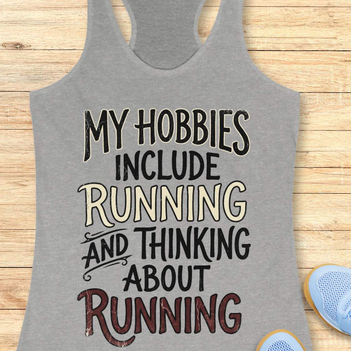 grey tank top with text 'My hobbies include running and thinking about running' on a wooden surface.