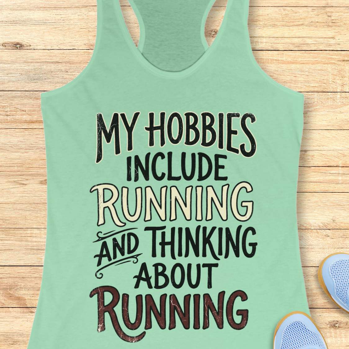 Mint green  tank top with text 'My hobbies include running and thinking about running' on a wooden surface.