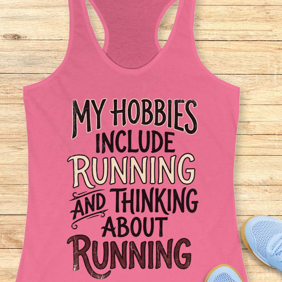 Pink tank top with text 'My hobbies include running and thinking about running' on a wooden surface.
