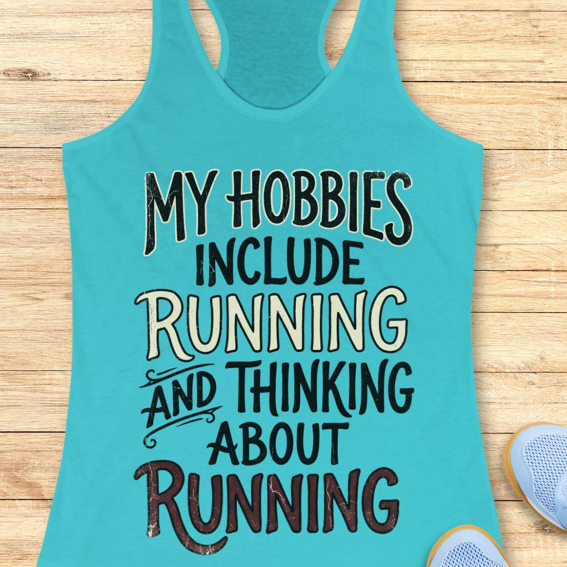 Turquoise tank top with text 'My hobbies include running and thinking about running' on a wooden surface.