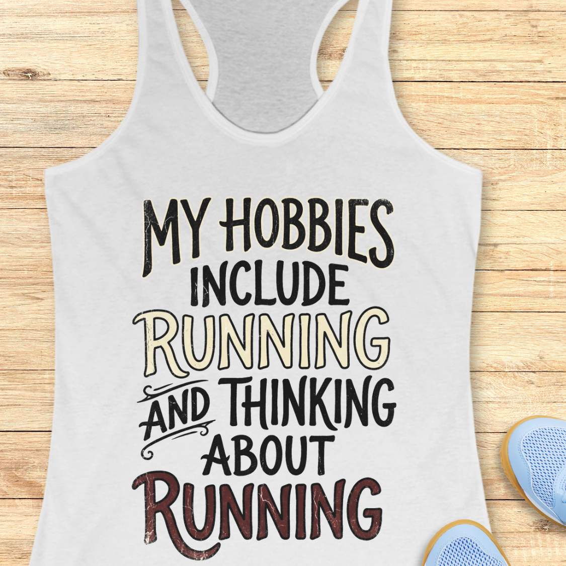 white tank top with text 'My hobbies include running and thinking about running' on a wooden surface.