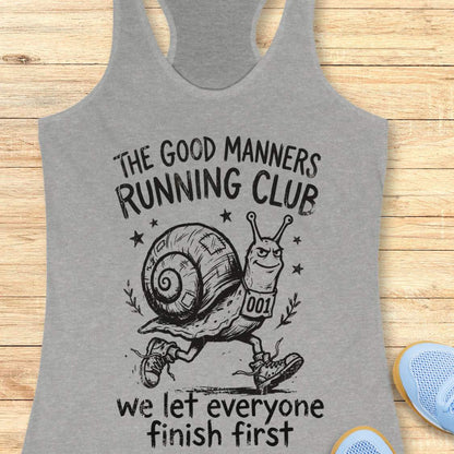 grey tank top with a snail graphic and text The good manners running club, we let everyone finish first, on a wooden surface