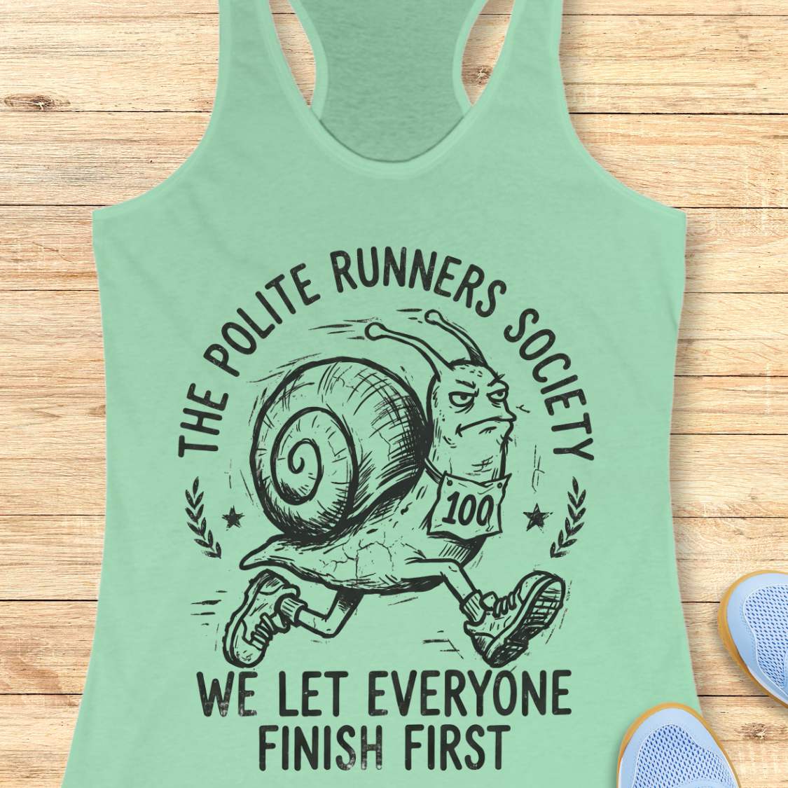 Light green tank top with a graphic of a snail and text 'The Polite Runners Society' on a wooden surface