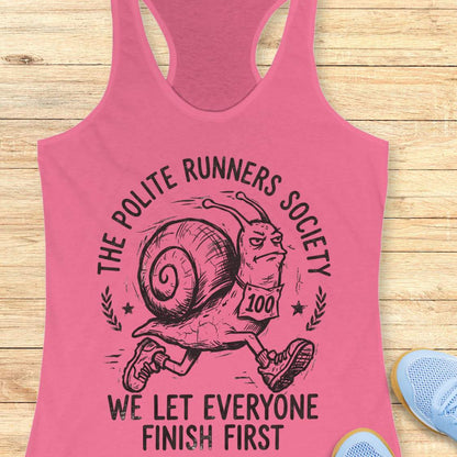 Pink tank top with a snail graphic and text 'The Polite Runners Society' on a wooden surface