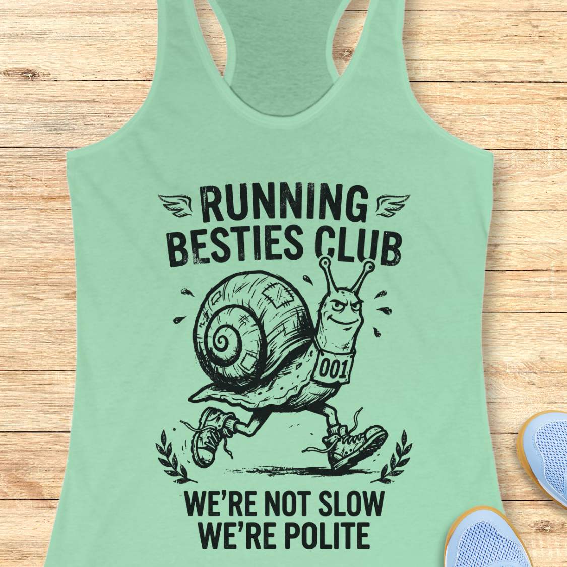 Light green tank top with a snail graphic and text  'Running Besties Club'  on a wooden surface