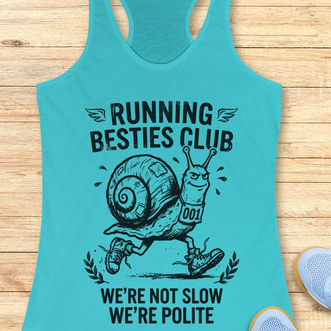 Turquoise tank top with a snail graphic and text  'Running Besties Club'  on a wooden surface
