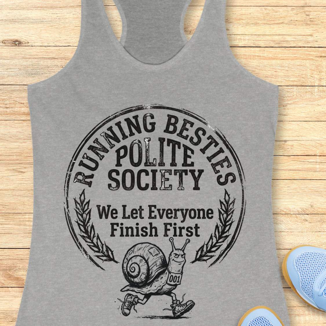 Gray tank top with 'Running Besties Polite Society' graphic on a wooden surface