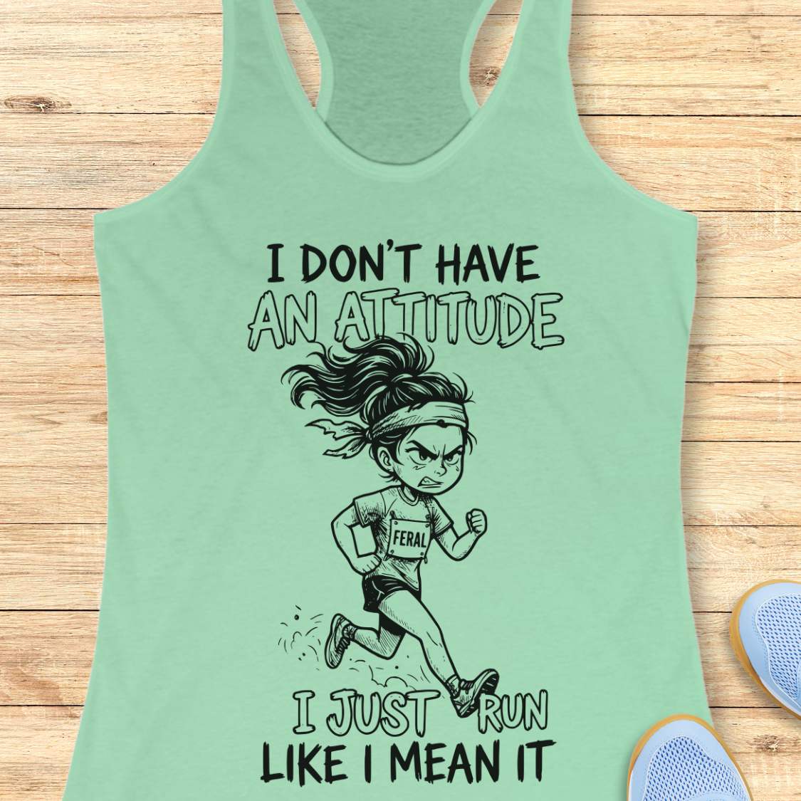 Mint green tank top with a graphic of a running girl and text I don't have an attitude, I just run like I mean it,  on a wooden surface.