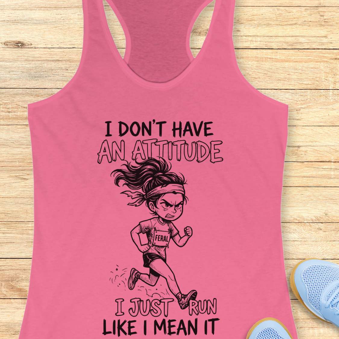 Pink tank top with a graphic of a running girl and text I don't have an attitude, I just run like I mean it,  on a wooden surface