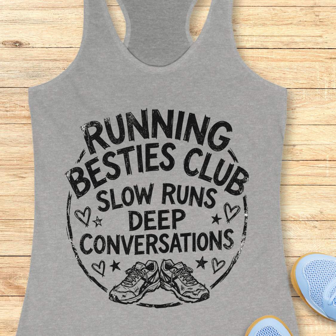 grey tank top with a graphic and text Running besties club, slow runs, deep conversations, on a wooden surface