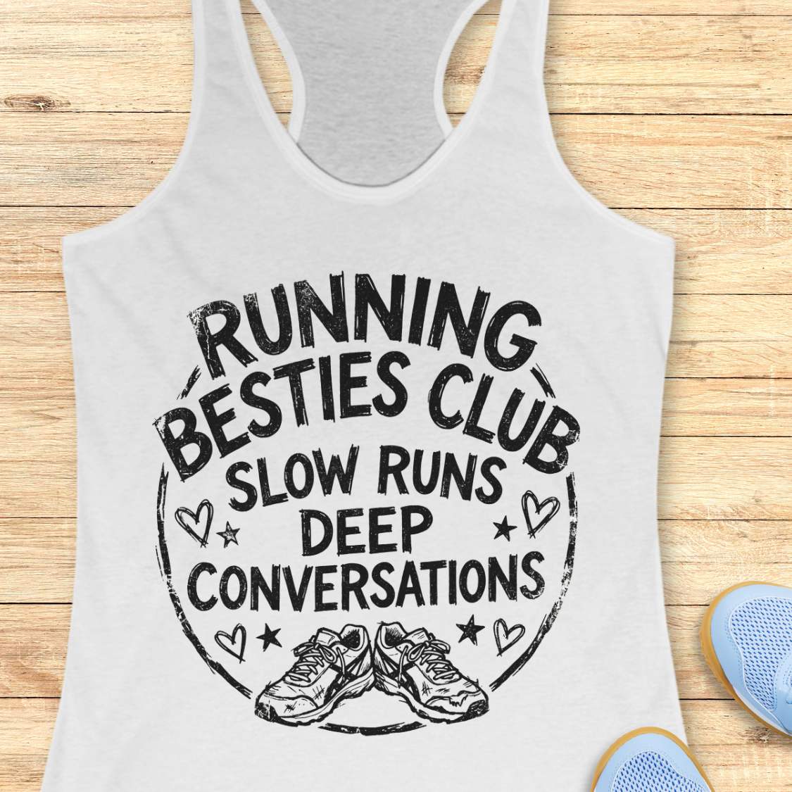 white tank top with a graphic and text Running besties club, slow runs, deep conversations, on a wooden surface