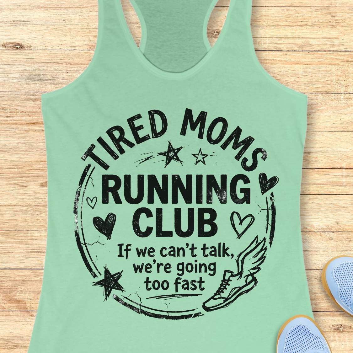 Mint green tank top with 'Tired Moms Running Club' text on a wooden surface