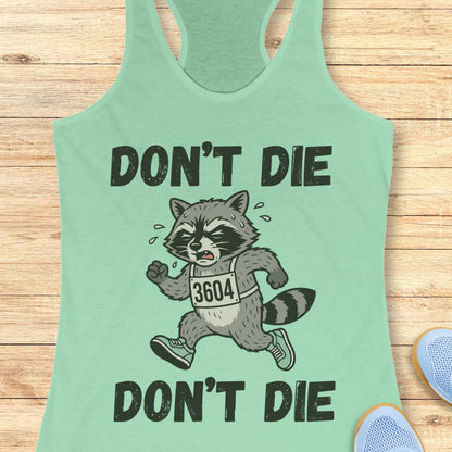 Light green tank top with a raccoon graphic and text 'Don't Die' on a wooden surface