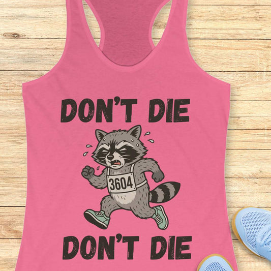 Pink tank top with a raccoon graphic and text 'DON'T DIE' on a wooden surface.