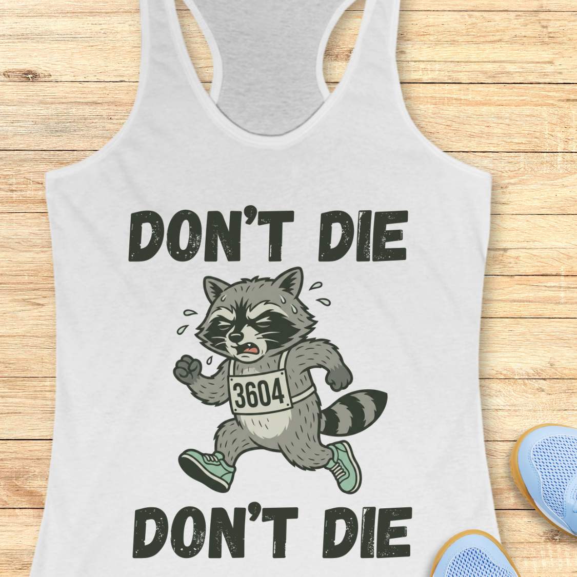 white tank top with raccoon graphic and text 'DON'T DIE' on a wooden surface