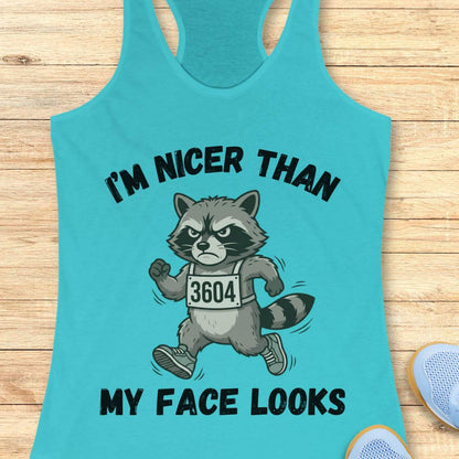 Turquoise tank top with raccoon graphic and text I'm nicer than my face looks, on a wooden surface