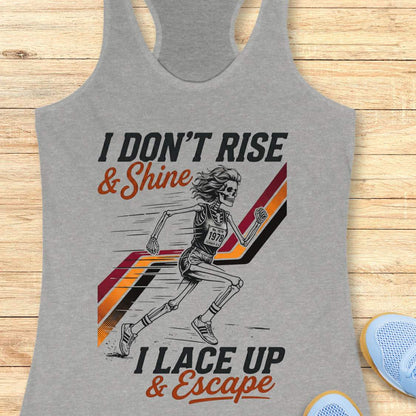 Gray tank top with graphic design of a runner and text I don't rise & shine, I lace up & escape, on a wooden surface
