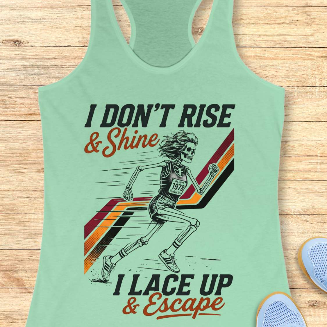 Light green tank top with graphic design and text I don't rise & shine, I lace up & escape, on a wooden surface