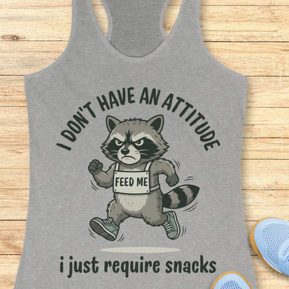 Gray tank top with a raccoon graphic and text I don't have an attitude, I just require snacks, on a wooden surface