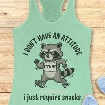 Mint green tank top with a raccoon graphic and text I don't have an attitude, I just require snacks, on a wooden surface