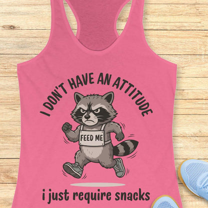 Pink tank top with a raccoon graphic and text I don't have an attitude, I just require snacks, on a wooden surface