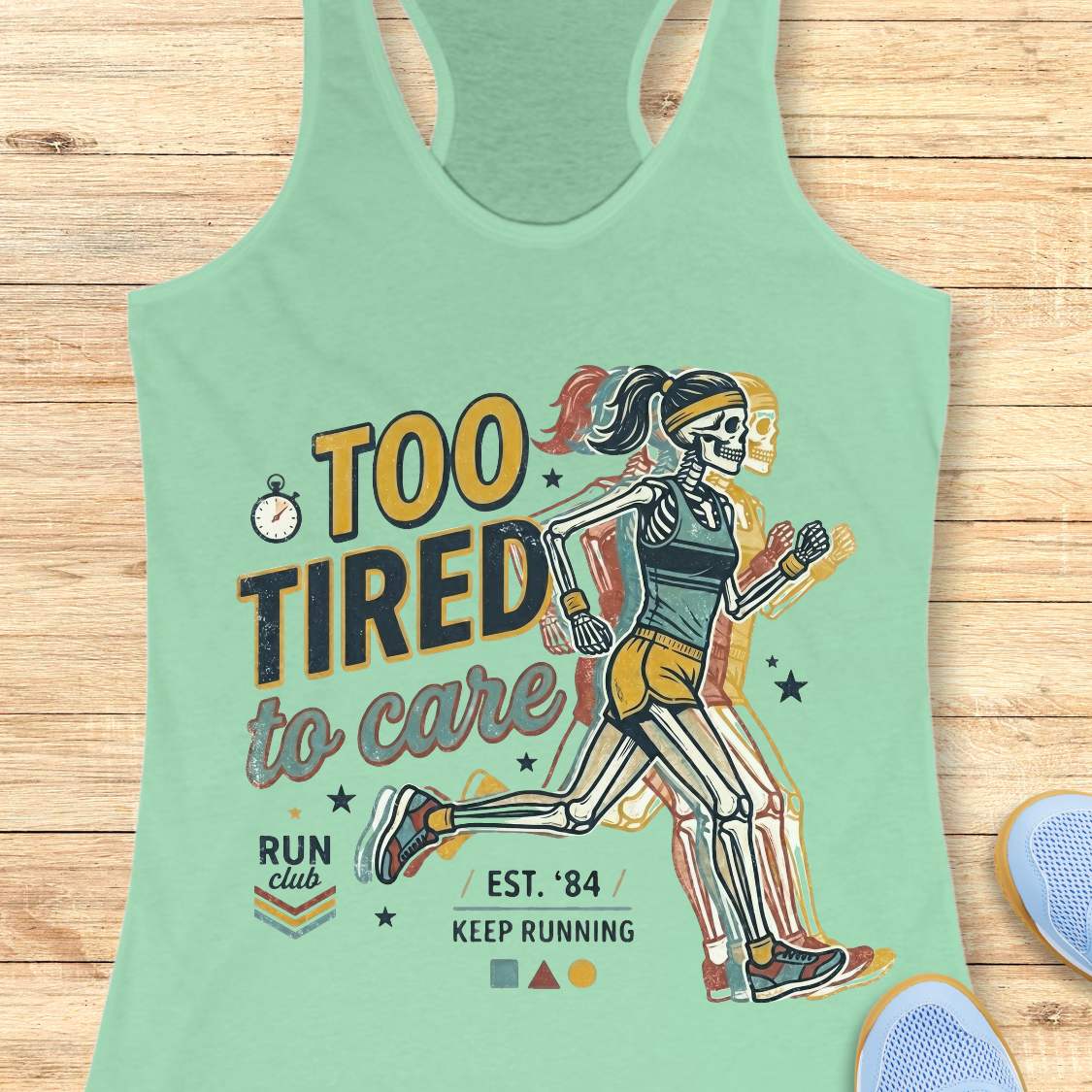 Mint green tank top with skeleton runner graphic and text  too tired to care run club, on a wooden surface