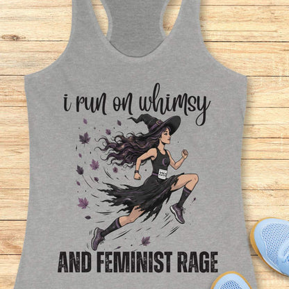 Gray tank top with a graphic of a witch runner and text  i run on whimsy and feminist rage, on a wooden surface