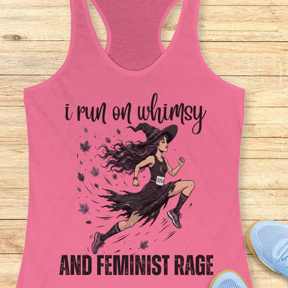 Pink tank top with a graphic of a woman running and text  i run on whimsy and feminist rage, on a wooden surface